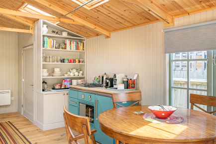 Hipped garden room interior by Crane Garden Buildings Garden building interior with fitted kitchenette, open shelving, dining table, timber floor and vaulted wooden ceiling with rooflights.
